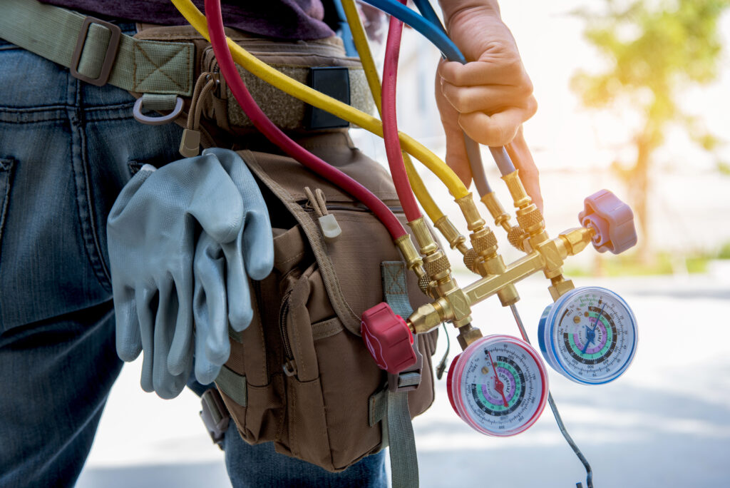 Close-up view of a technician's tool belt equipped with protective gloves and HVAC manifold gauge hoses in red, yellow, and blue, symbolizing professional maintenance, repair, and diagnostic work in heating, ventilation, and air conditioning systems.