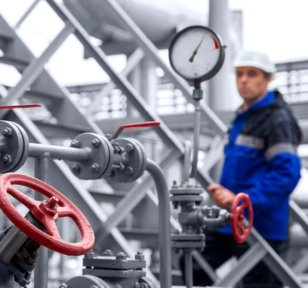 Industrial HVAC technician inspecting valves, piping, and a pressure gauge in a mechanical system.